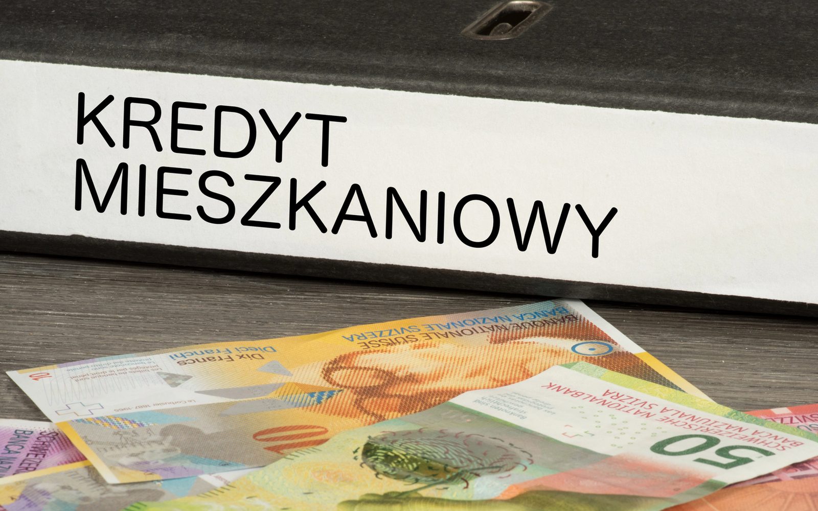 Segregator z napisem „Kredyt mieszkaniowy” na banknotach franka szwajcarskiego